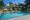 The Maidens in Delhi India a rectangular pool in the centre has grey paving all around an on one side a 5 groups of 2 yellow sun loungers with umbrellas over, and beyong the grass behind is a long one story white building