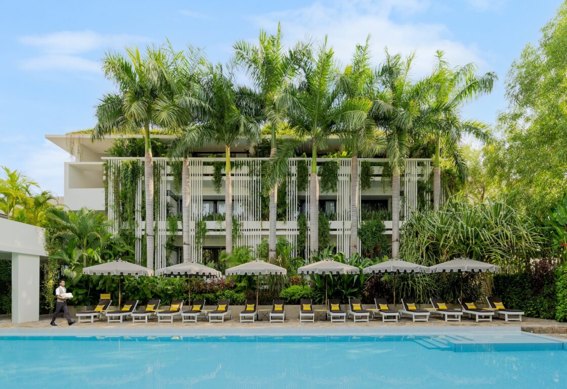 Viroth's Hotel in cambodia a white building with a pool and loungers stretching out in front and with tall palm trees growing in front