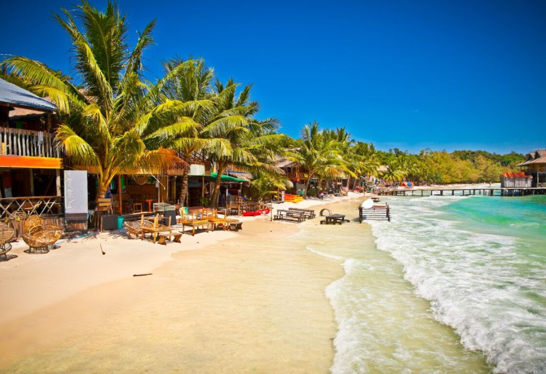 shops and huts along a stretch of perfect sand with crystal clear sea crashing onto the shore in koh rong, cambodia
