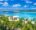 view of a beach front resort in the maldives surrounded by white beaches, palm treas and turquoise waters