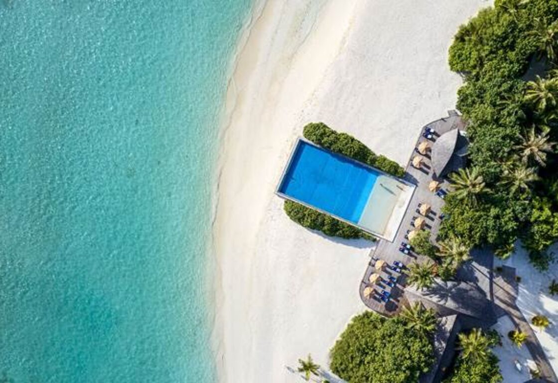 aerial shot of a beach front hotel in Maldives reaching out all the way to the ocean with crystal clear waters and sandy beach