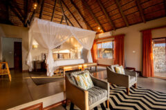 a large luxury safari room with two armchairs, striped rug, large bed in the background with white sheer mosquito nets