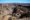 Vast desert canyon with steep rocky cliffs and a dry riverbed cutting through layered stone under clear blue skies.