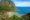 Cauayan Island Resort in the Philippines view from on top of a hill looking down on the beach and forest below and the tops of pointed roofs can be seen along the beach and on the right hand side there are 4 separate huts over the water