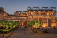 Historic Chanoud Garh heritage hotel in Rajasthan, India, illuminated at dusk with traditional Rajput architecture, ornate balconies, courtyards and landscaped gardens.