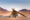 A-frame desert chalet at Desert Quiver Camp, set on open plains with distant mountains under clear skies.
