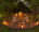 a front view of a safari lodge featuring terrace with two chairs and a table set in a woodland at dusk
