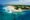 Wild beach peninsula with white sands, further back lush green vegetation and a crystal clear teal blue sea.