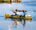 Two people paddling away in a yellow sea kayak with still waters.