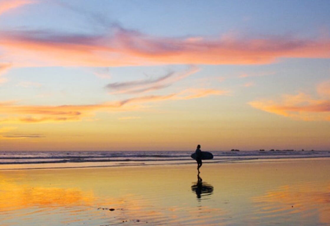 a silhouette of a surfer walking in the ocean at sunset