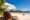 two wooden lounge chairs with blue cushions and white sun brolly located right on the sandy beach and nearby the ocean