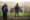 A group of people with backpacks observe a rhinoceros in a grassy landscape. The scene feels tense yet awe-inspiring, highlighting wildlife tourism.