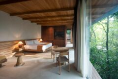 inside of a bungalow at Rio Perdido with large open space, large bedroom with brown throw blanket, two side lamps, coffee table and floor to ceiling window leading onto terrace