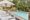 A serene outdoor pool area with white lounge chairs and umbrellas lined up alongside a clear blue pool. Lush greenery and a cozy patio in the background.