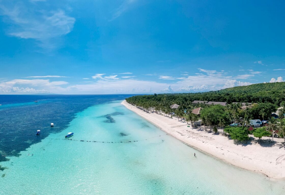 Panoramic view of the coastline of Panglao island in Bohol in the philippines with white sand and crystal clear sea with palm trees along the coast and the roofs of buildings dotted around
