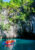 a small boat in the philippines takes a group of tourists in orange life jackets along water towards a large hole in the side of a cliff that has trees growing all along the top