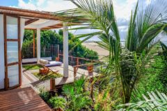 a view of a pation with corner wooden terraces feturing chairs and ocean views with green palm trees around
