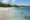 A white sandy beach stretching round into a bay with shimmering blue turquoise sea. On the borders of the beach are lush green tropical trees.