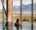 Woman in an infinity pool, looking out of floor to ceiling windows at snow capped mountains and a lake in the distance