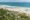 an aerial view of a beach front resort fringed by palm trees set on the edge of a beach and ocean
