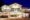 Villa Caemilla Boracay in the philippines a white building with two pointed roofs on one end and on the other side a flat roof over a terrace sits on sand with a night sky and on the sand to the left are black tables and chairs underneath some umbrellas