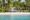 Villa Caemilla Boracay in the philippines an image taken from the sea looking at a dense forest full of palm trees and in the middle there is a clearing and from that clearing a building with pointed roofs and a line of umbrellas on the sand can be seen