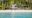 Villa Caemilla Boracay in the philippines an image taken from the sea looking at a dense forest full of palm trees and in the middle there is a clearing and from that clearing a building with pointed roofs and a line of umbrellas on the sand can be seen