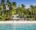 Villa Caemilla Boracay in the philippines an image taken from the sea looking at a dense forest full of palm trees and in the middle there is a clearing and from that clearing a building with pointed roofs and a line of umbrellas on the sand can be seen