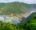 A lush green hillside overlooks a curving train bridge crossing a river mouth that meets the ocean.