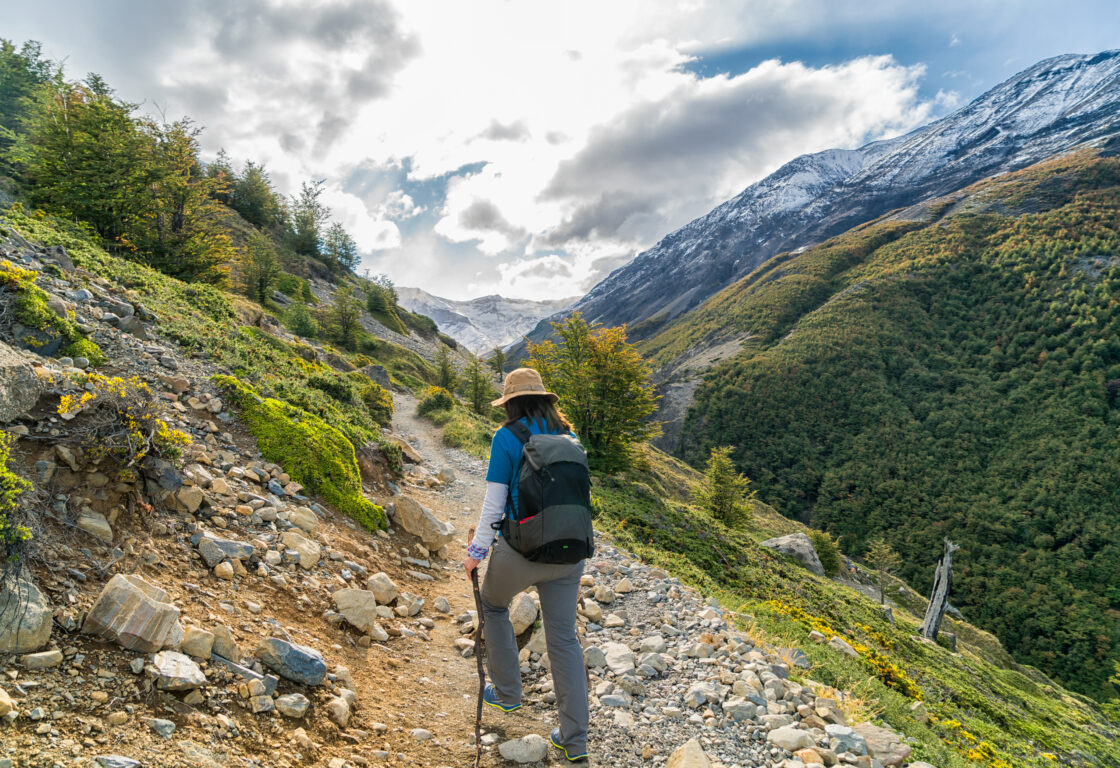 a woman dressed in hiking clothes with a little hat hiking W Trek to Lake of Torres del Paine National Park, Patagonia, Chilie