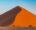 a large sand dune in namibia shaped in a triangle shape at sunset looking almost orange