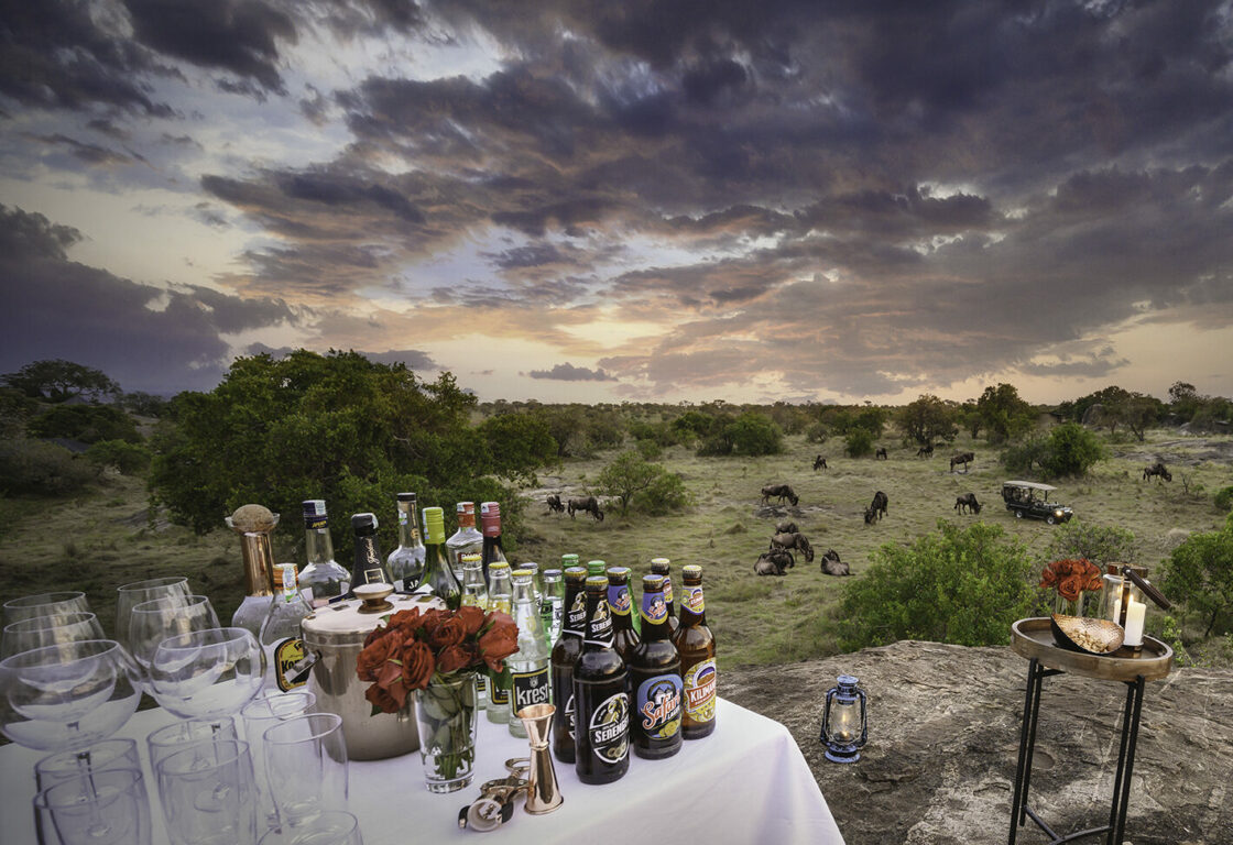sundowner drinks in the bush, table full of drinks and glasses, set up in the middle of the bush at sunset