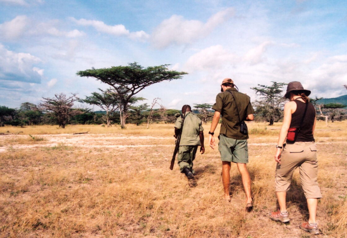 a walking safari in the bush, a ranger with a gun at the front, two people following