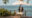 a couple standing on a terrace with a white umbrella overlooking the ocean