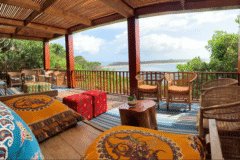 bedroom terrace in wooden style with two chairs, red futton, yellow and orange print blankets