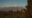 a view across the tops of a vineyard with the odd tree standing tall but in the distance are snow capped mountains and a clear blue sky