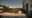 along the bottom of the image is a pool with fountains going into the water and on the right is a white building with an arch way and tall window and opposite the pool on a patio overlooking trees and vines