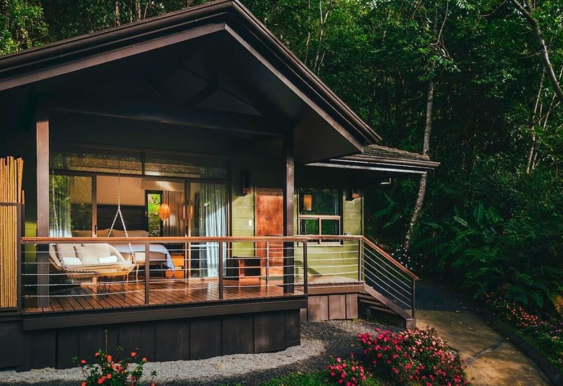 A small wooden cabin nestled in the woods, featuring a charming balcony overlooking the surrounding trees.