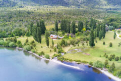 aerial view above a lake and a green landscape with trees and in a clearing a wooden building