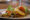 a white plate has some fish in the middle and on top of the fish is sliced carrots and lemon with some watercress