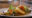 a white plate has some fish in the middle and on top of the fish is sliced carrots and lemon with some watercress