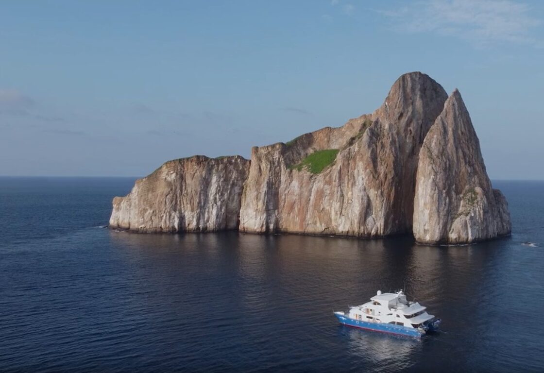 A boat crusining on a calm empty sea with a rocky outcrop behind it