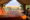 a view of a tented lodge with large double bed, cushions and red blanket, overlooking the African bush and savannah