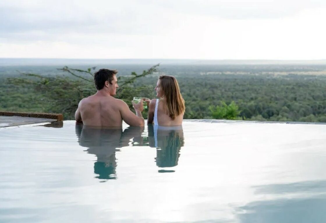 a couple in an infinity pool overlooking the african savanna - honeymoon in Kenya