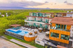 an aerial view of Iguana-Crossing. Galapagos featuring large three floor building with blue and white walls, red roof, large swimming pool and terraces overlooking the beach and ocean