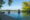 picture taken water level of an infinity swimming pool with a woman at the edge of the pool overlooking a flat, blue river and on the other side is a green bank lined with trees