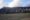 in the background is a tall hill with a grey side covered in ridges and at the base is a line of trees and then a space of dark grey sand at Mount Bromo in indonesia