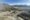 mountainous ridges run along the back of the photo and grey stone. people walk up ad down a wooden staircase along the middle of the picture and they show just how small they are in the space around them at mount bromo in indonesia