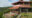 a view of a lodge with pinkish walls and red tile roof, large outdoor terrace, perched on a hill in the green area