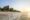 Beachfront view at sunset with thatched-roof huts lined along the sandy shore and gentle waves in the foreground.